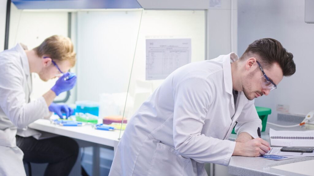 students in lab coats writing notes and preparing experiment