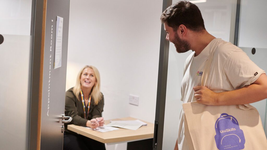 A student is entering a room to talk to a uniskills advisor who is sat inside smiling at the open door