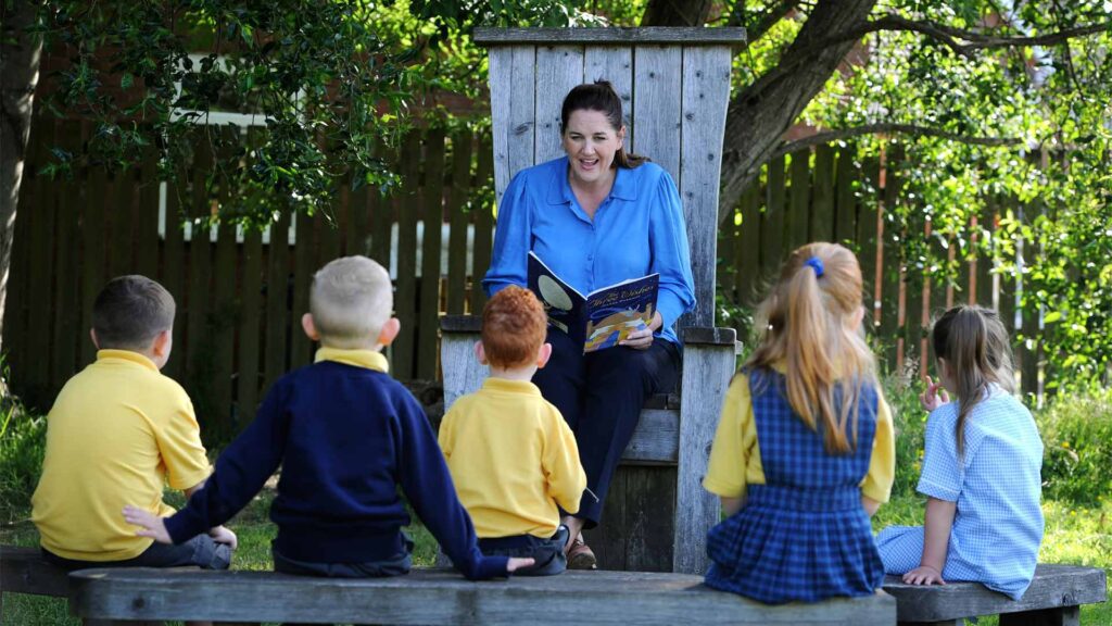 A trainee teacher reads to primary school children in Forest School