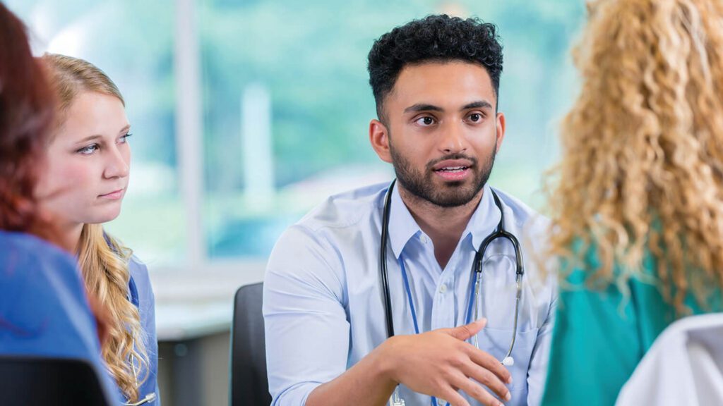 A doctor talks to colleagues during a meeting.