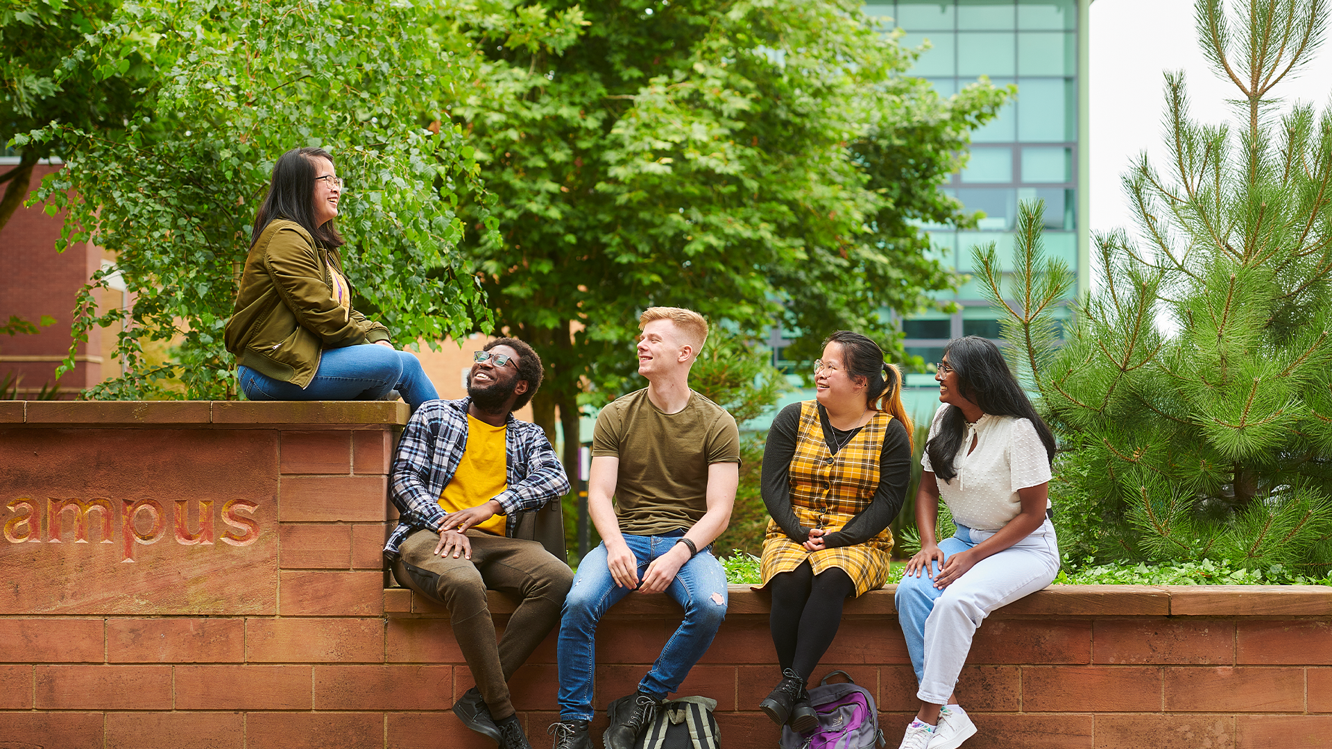 group of students sat outside on a wall on campus