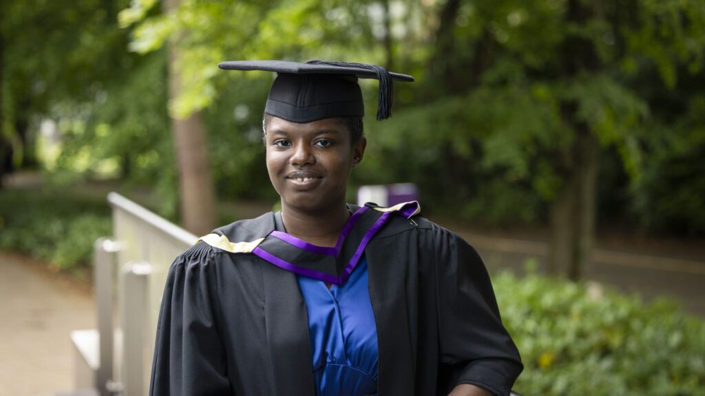 Racheal wears a graduation hat and gown and smiles at the camera.