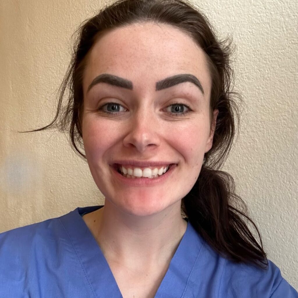 Jade Ainsworth wears blue scrubs and smiles at the camera.