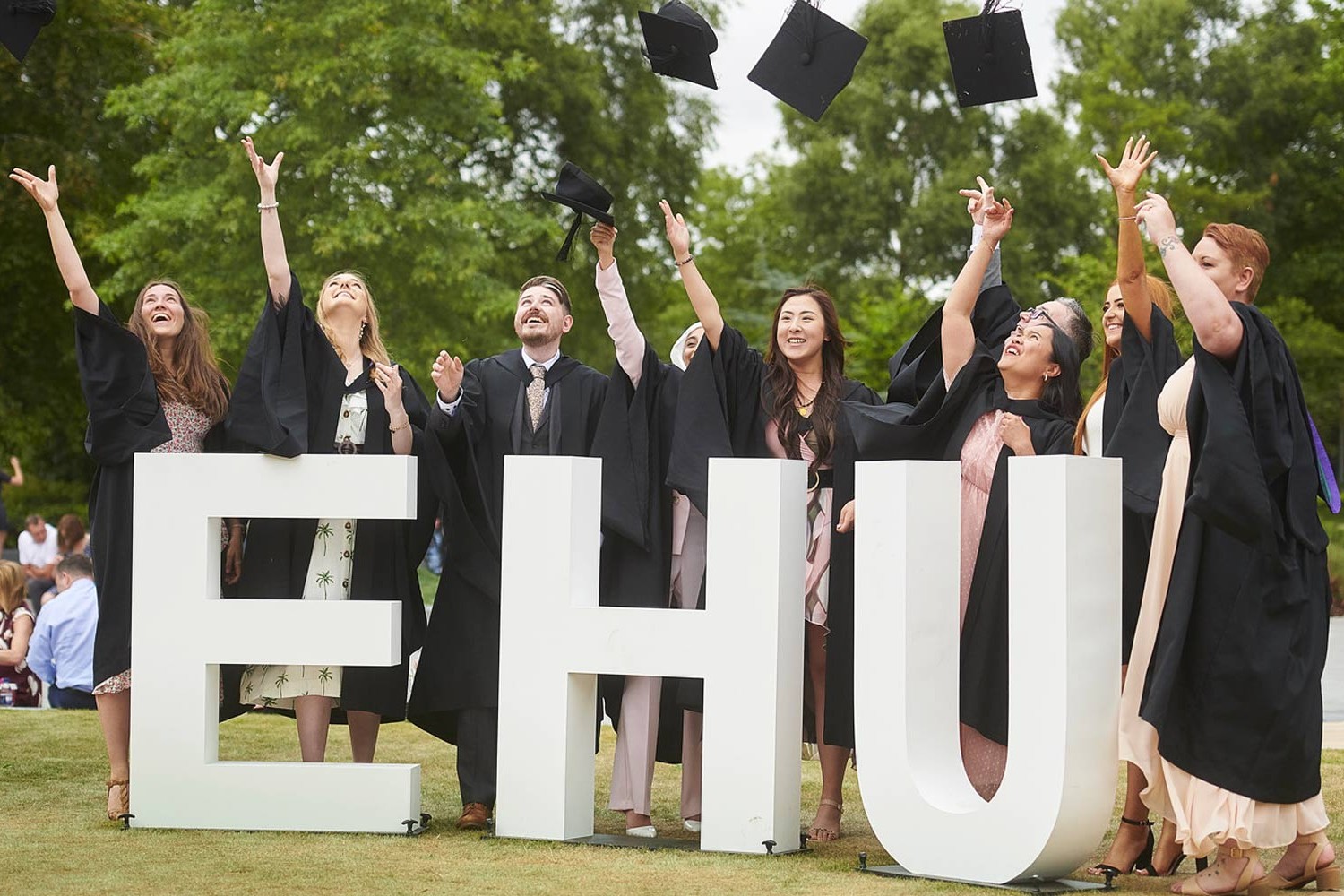 Group of students at graduation, standing next to white EHU letters and throwing their caps into the air