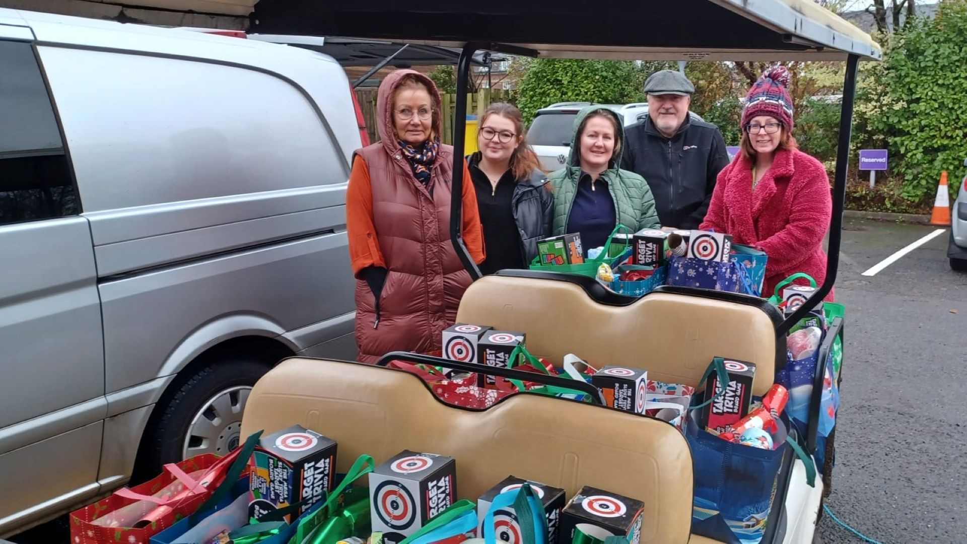 A group of five staff and helpers smiling and standing in front of a golf buggy filled with gift hampers for student care leavers