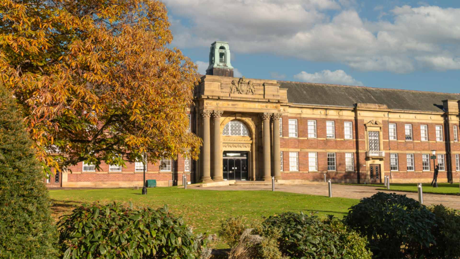 A photograph of the main building entrance and green in Autumn.