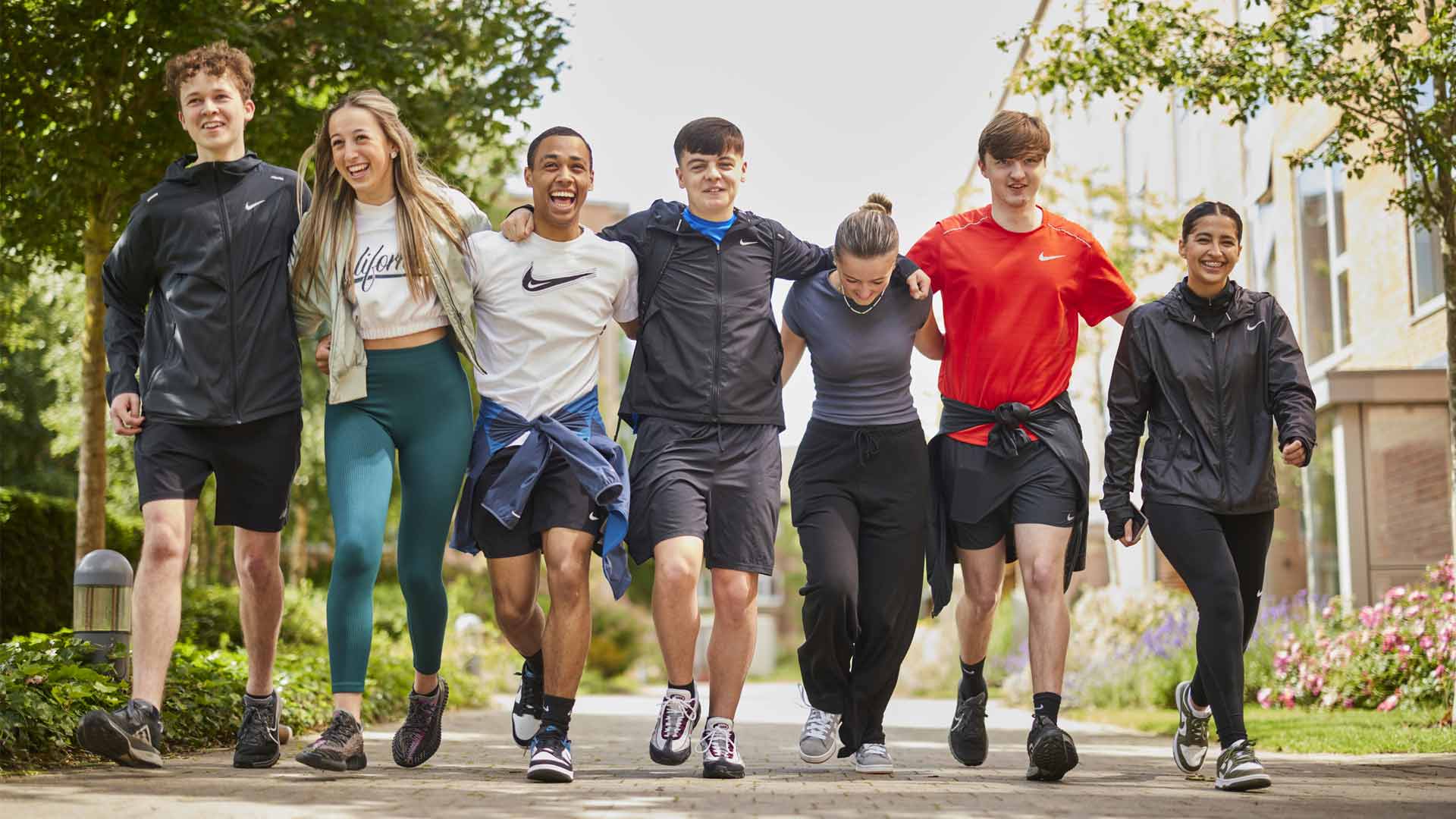 a group of happy students, linking arms and walking through campus