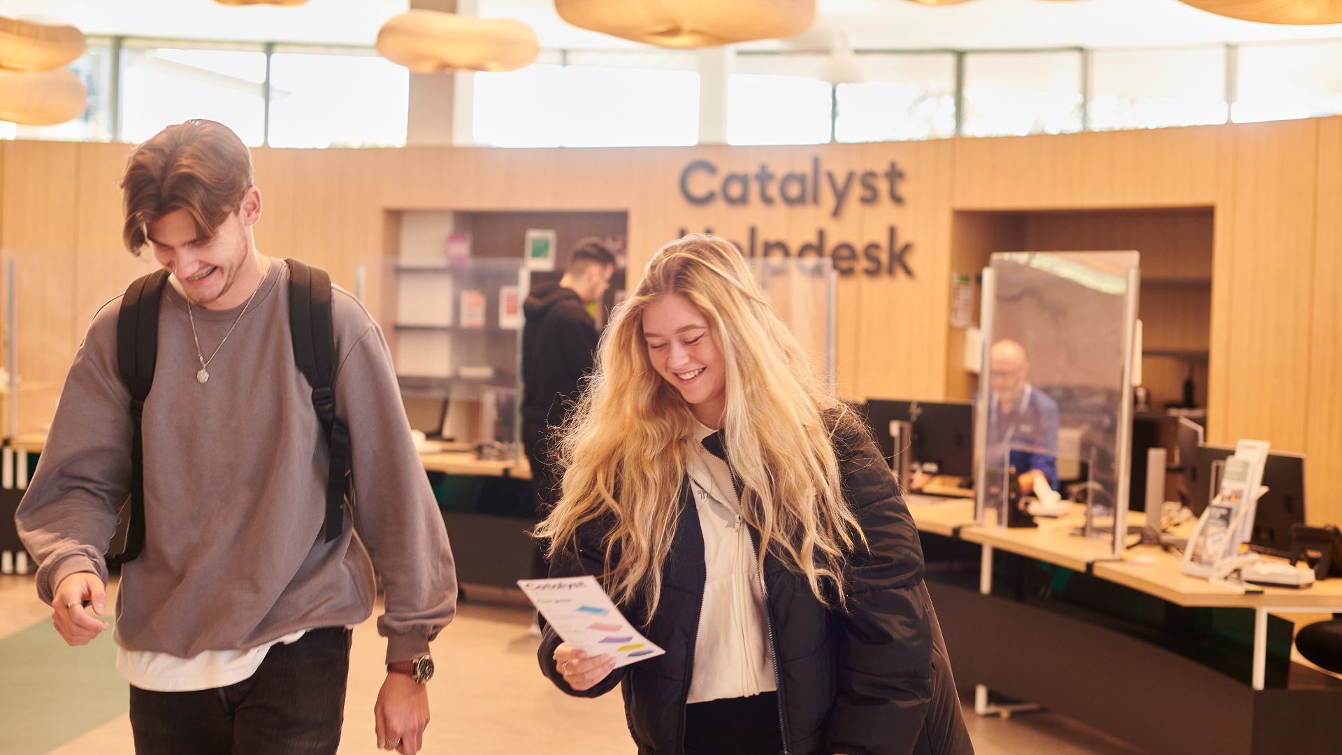 Two students walking in Catalyst reading a leaflet