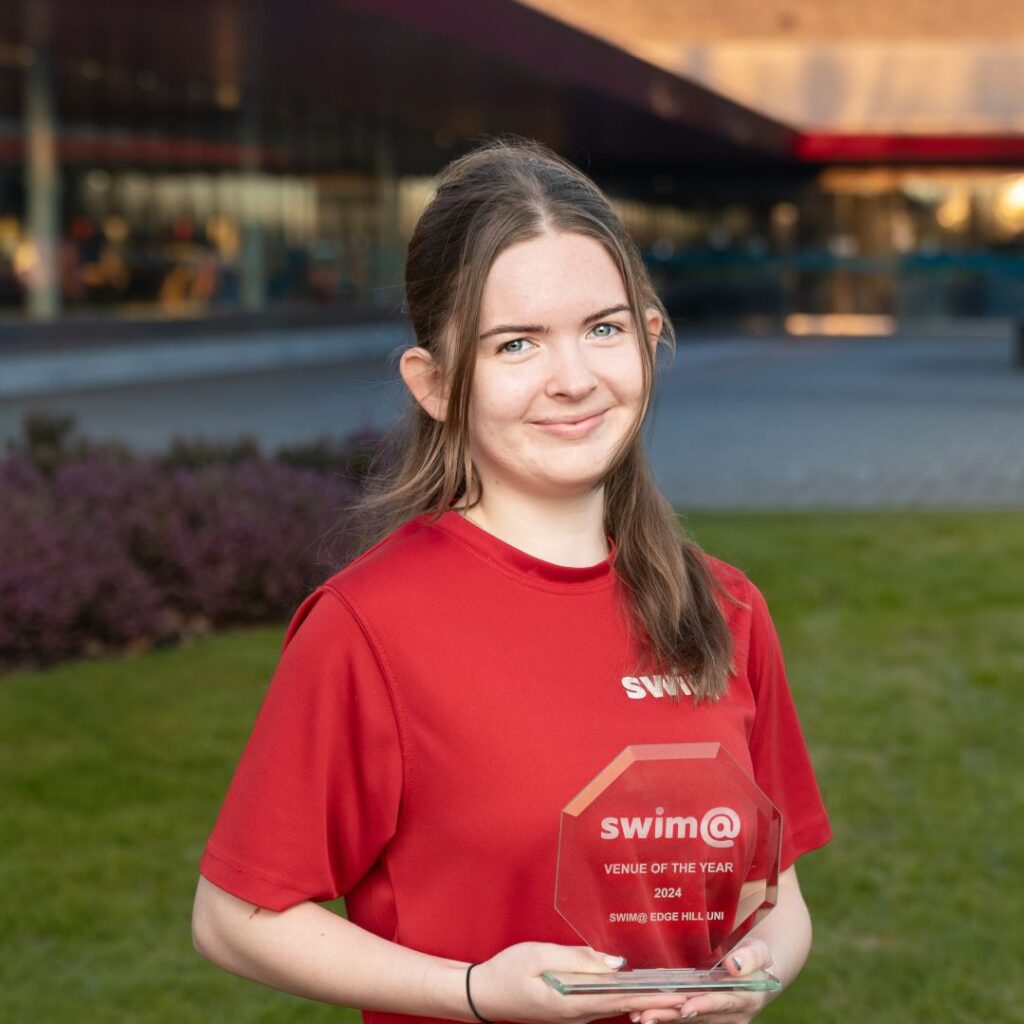 Clare Parker stands on grass and holds the swim! 'venue of the year' trophy.